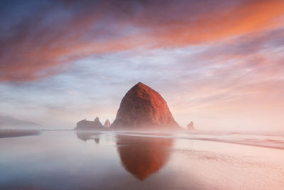 Rock formation in sea against sky during sunset