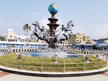 Statue by fountain against buildings in city against sky