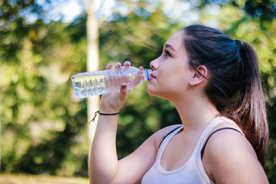 Side view of woman drinking water while standing at park