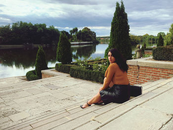 Young woman sitting by plants against trees against sky