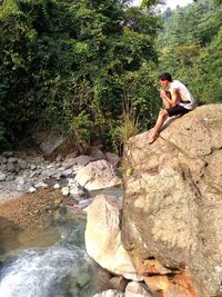 Young woman sitting on rock by tree