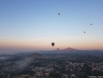 Hot air balloons flying in city against sky during sunset