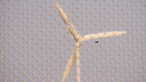 Windmill seen through chainlink fence against clear sky