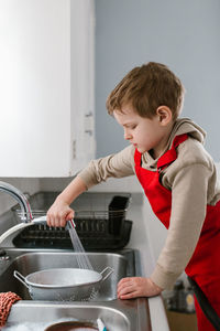 Side view of boy cleaning colander in kitchen sink