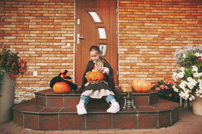 Little girl dressed as a fairy with a lantern jack sits on the steps near her house during