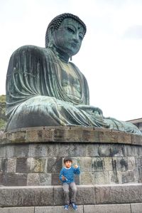 Boy sitting against giant buddha statue at kotoku-in temple