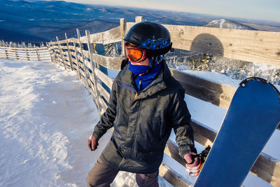 Man holding snowboard standing on snow covered field during winter