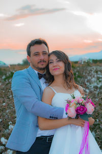 Portrait of smiling bride and groom with bouquet romancing on field