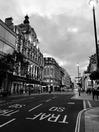 View of city street and buildings against cloudy sky