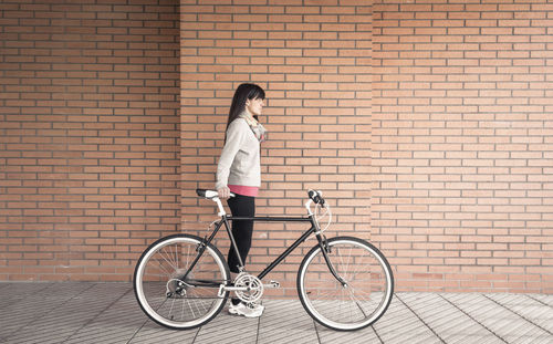 Woman with bicycle standing against brick wall