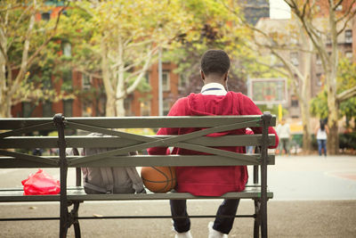 Rear view of student sitting on bench at basketball court