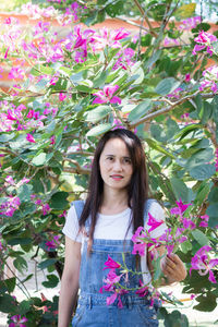 Portrait of woman with pink flower standing against plants