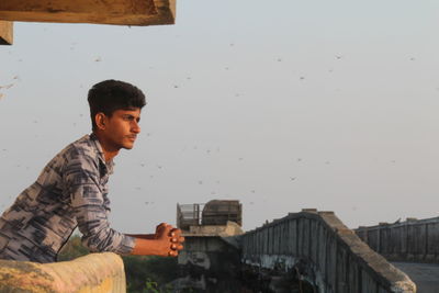 Side view of young man looking away against sky