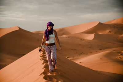 Tourist woman wearing a purple turban walking on a dune in the sahara desert
