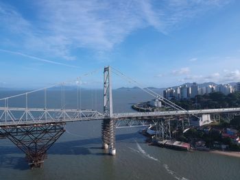 Suspension bridge over sea against cloudy sky