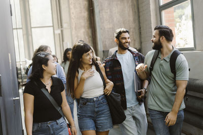 Happy multiracial male and female friends walking in college corridor