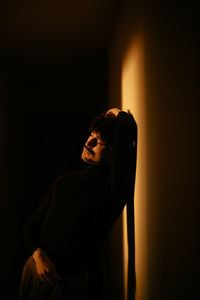 Young man with mustache sitting next to wall and running fingers through hair while tilting head down with closed eyes