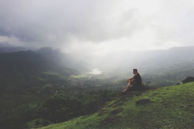 Man sitting on mountain against sky