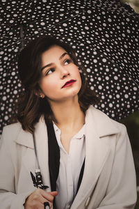 Woman looking away while holding umbrella