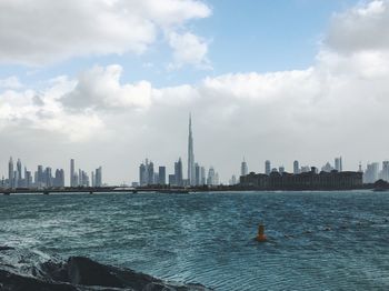 City at waterfront against cloudy sky