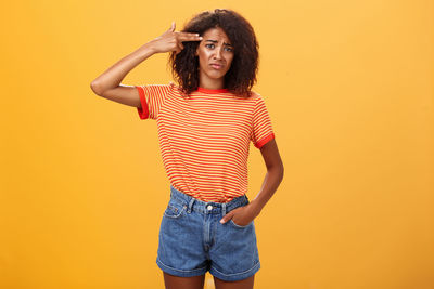 Portrait of young woman standing against yellow background