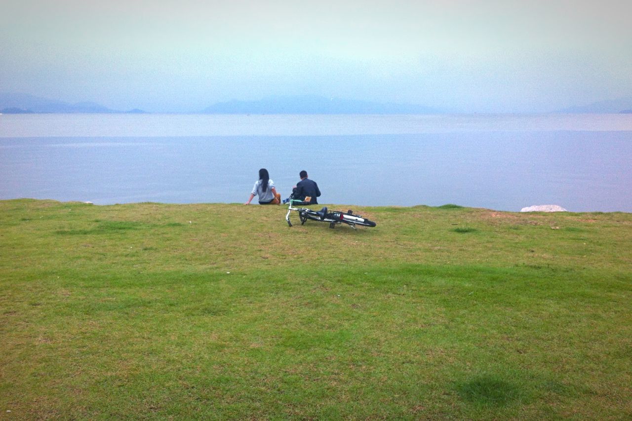 lifestyles, leisure activity, men, togetherness, grass, sea, horizon over water, sky, transportation, water, nature, beauty in nature, bonding, mode of transport, sitting, tranquility, full length, scenics