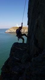 People on rock by sea against clear sky