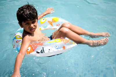 Happy indian boy swimming in a pool, kid wearing swimming costume along with air tube during day