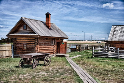 Barn on field by houses against sky