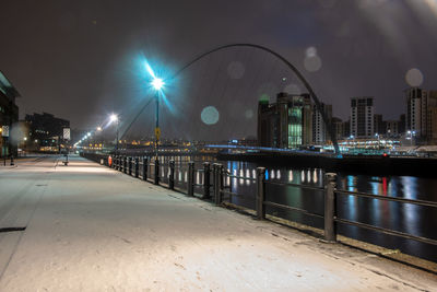 Illuminated bridge over river by buildings against sky at night