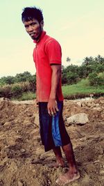 Portrait of young man standing on field against sky