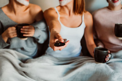 Midsection of friends watching tv while sitting on sofa at home