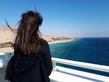 Rear view of young woman standing in boat by sea against sky