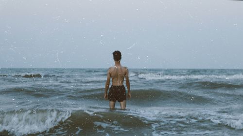 Rear view of shirtless man standing in sea against sky