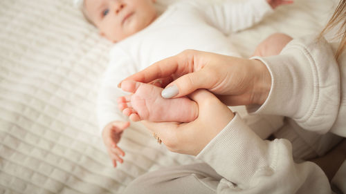 Mother massages her little daughter, newborn baby. lies on bed in bedroom, homely. legs, fingers. 