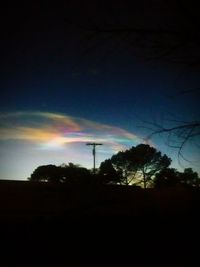 Low angle view of silhouette trees against rainbow in sky