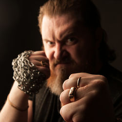 Close-up portrait of man holding hands against black background