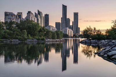 Reflection of trees and buildings in lake during sunrise