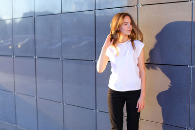 Portrait of young woman standing against wall