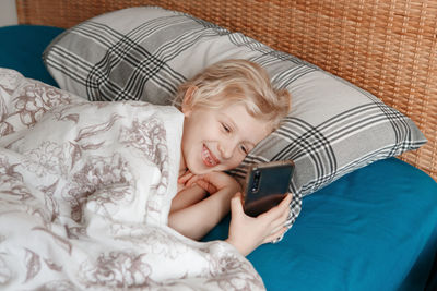 Cute girl lying in bed in morning and texting talking in social media on smartphone cellphone. 