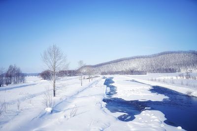 Snow covered landscape against clear blue sky