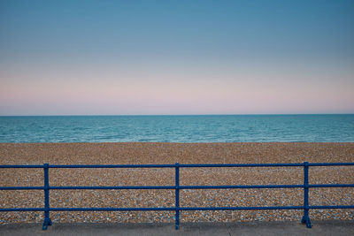 Blue painted metal railings in front of open, empty, shingle beach on eastbourne promenade.