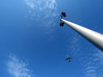 Low angle view of street light against airplane flying in sky