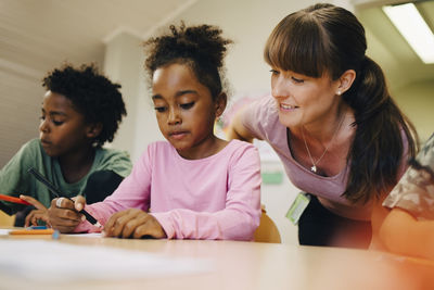 Smiling female teacher looking at students drawing in class