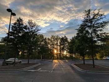 Road amidst trees against sky at sunset