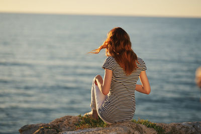 Woman looking at sea shore against sky during sunset