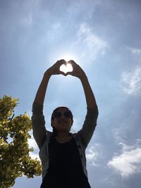 Low angle view of woman making heart shape against sky