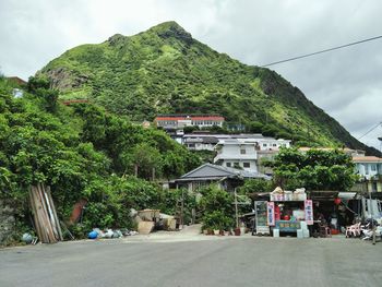 Houses by road amidst trees and buildings against sky