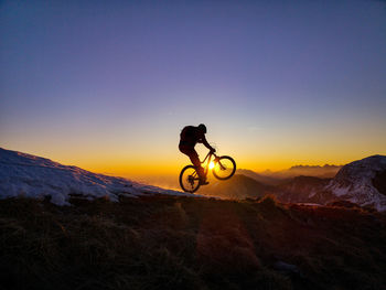 Silhouette person with umbrella on mountain against sunset sky