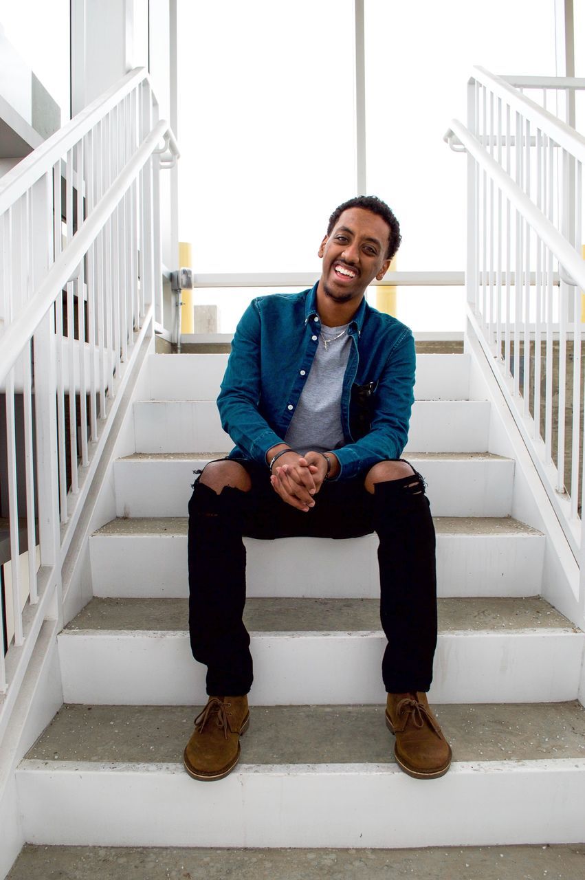 PORTRAIT OF A SMILING YOUNG MAN SITTING ON FLOOR